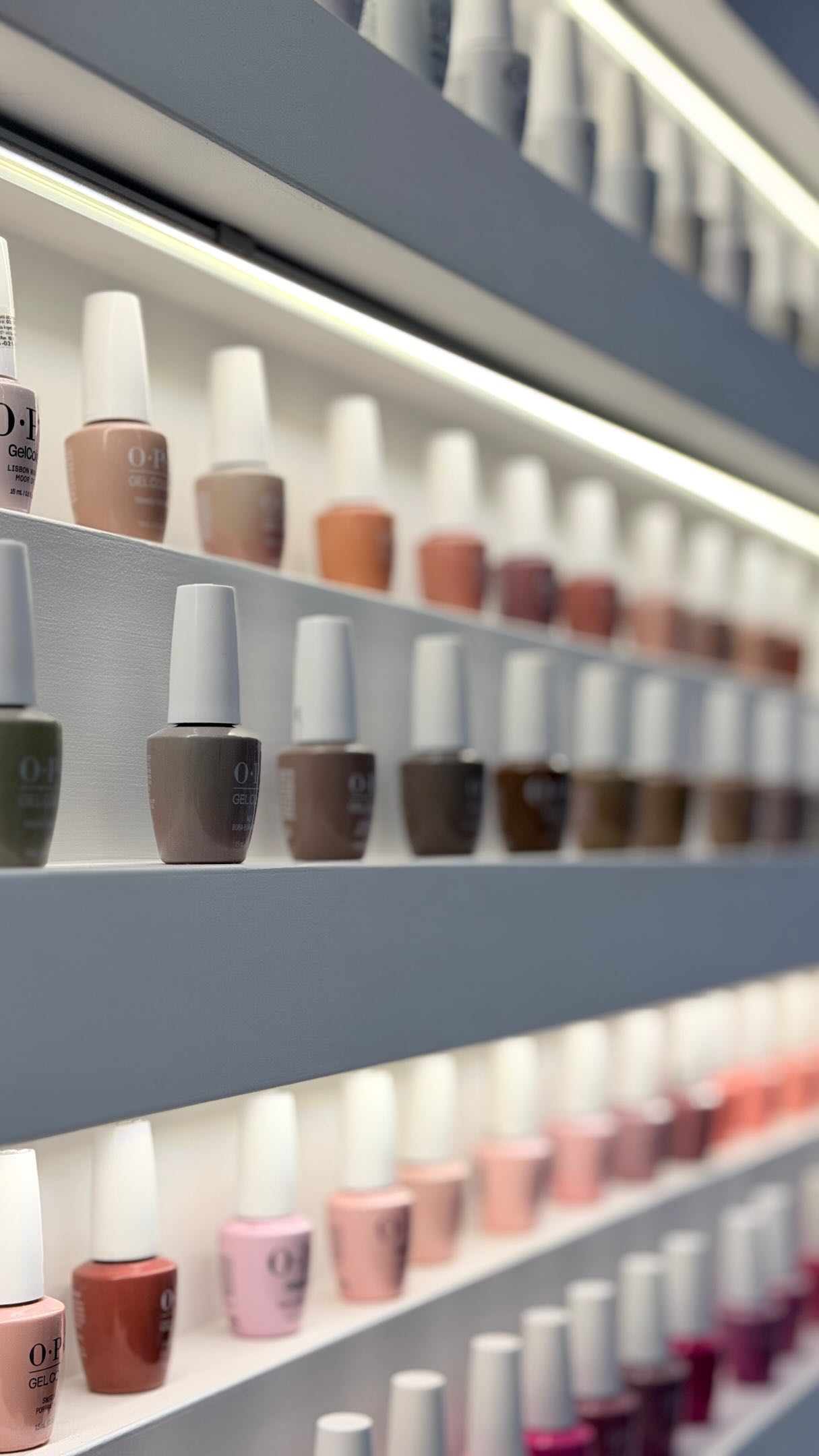 Estantes iluminados con frascos de OPI GelColor ordenados por tono, de nudes a marrones y rosas