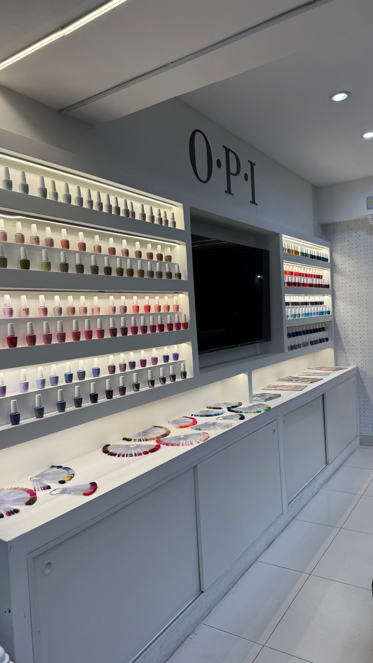 El muro de colores OPI GelColor de BeautyTam: estantes iluminados con frascos de todos los tonos y el mostrador con los muestrarios